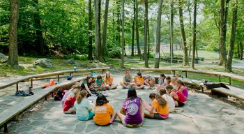 Campers sitting outdoors in a circle playing music